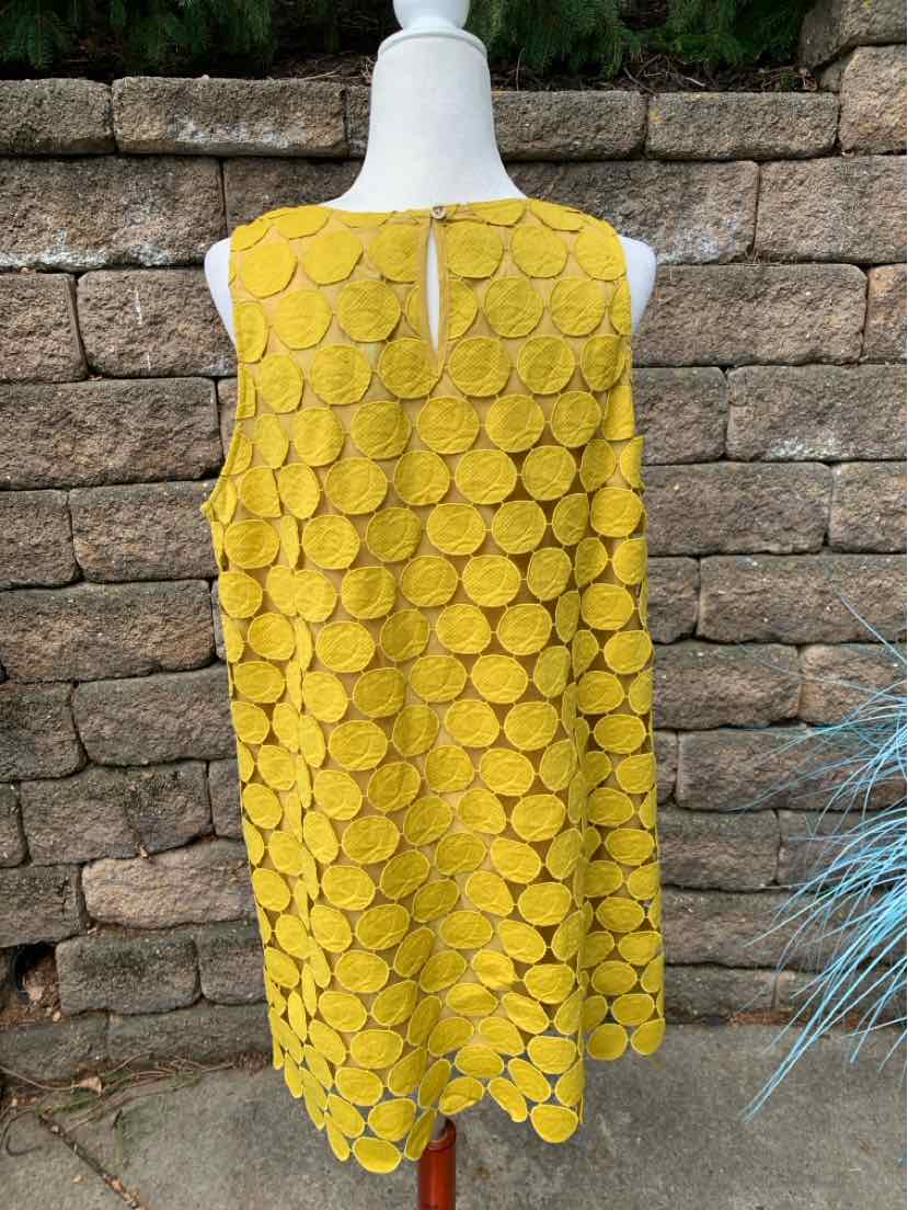 Sleeveless mustard yellow dress with circular textured pattern and keyhole back detail on mannequin.