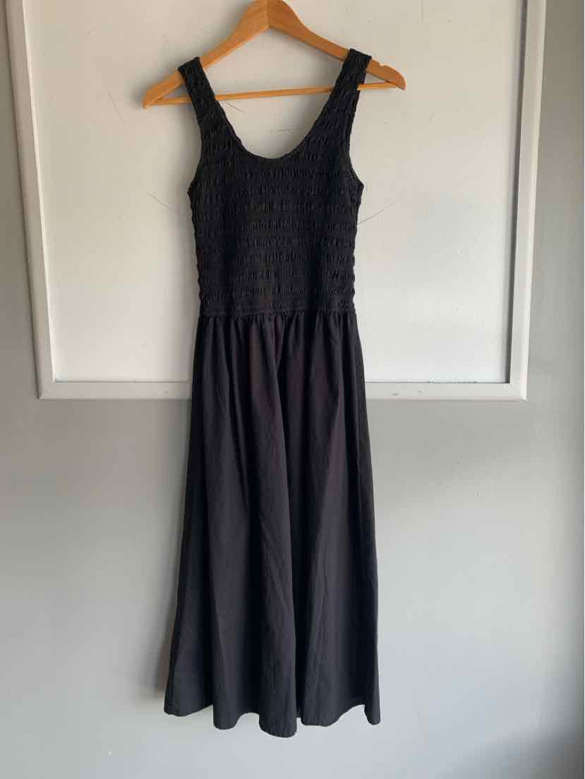 Black sleeveless dress with textured fitted bodice and flowy midi skirt on wooden hanger.