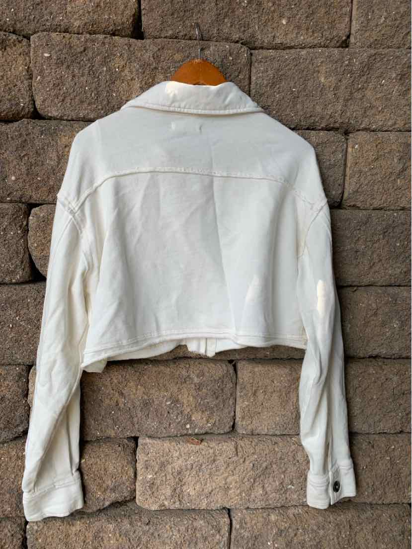 Cropped white jacket with long sleeves and wide collar hanging against stone wall.