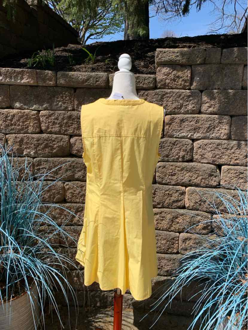 Yellow sleeveless knee-length dress with pleated skirt on mannequin against stone wall background.
