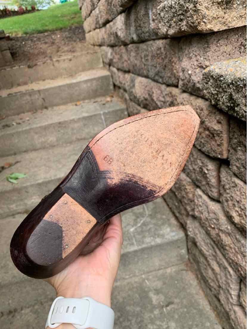 Brown leather western boot sole with a worn pointed toe and smooth heel.