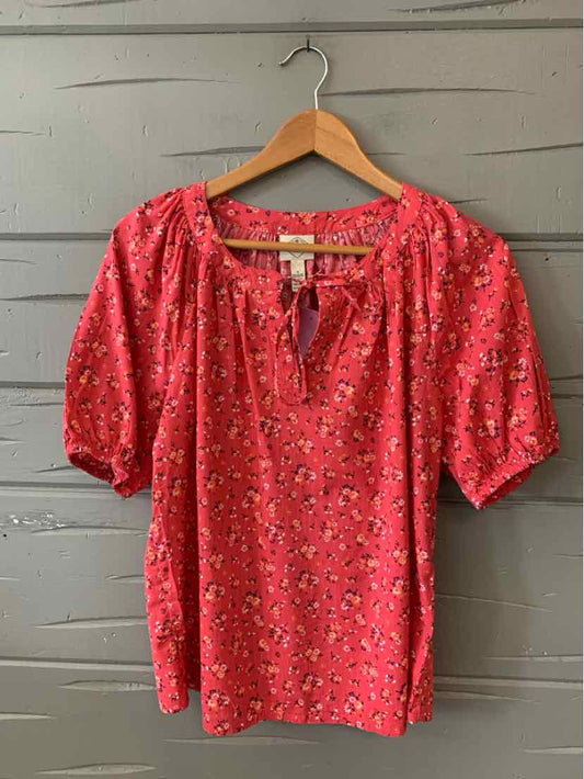 Pink floral blouse with puff sleeves and keyhole neckline on wooden hanger.