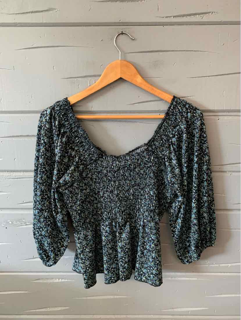 Black long-sleeve blouse with small white floral print, scoop neckline, and gathered waist detail.