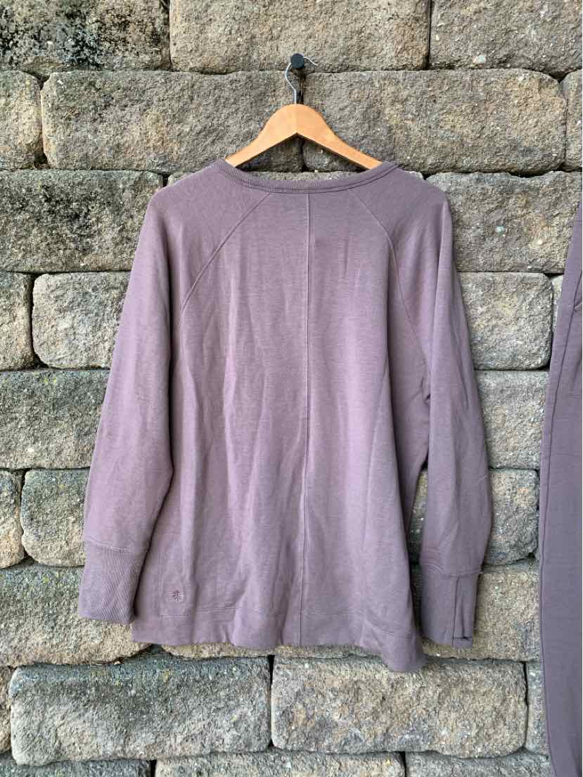 Mauve long-sleeve athletic top with crew neckline and relaxed fit, hanging on wooden hanger against stone wall.