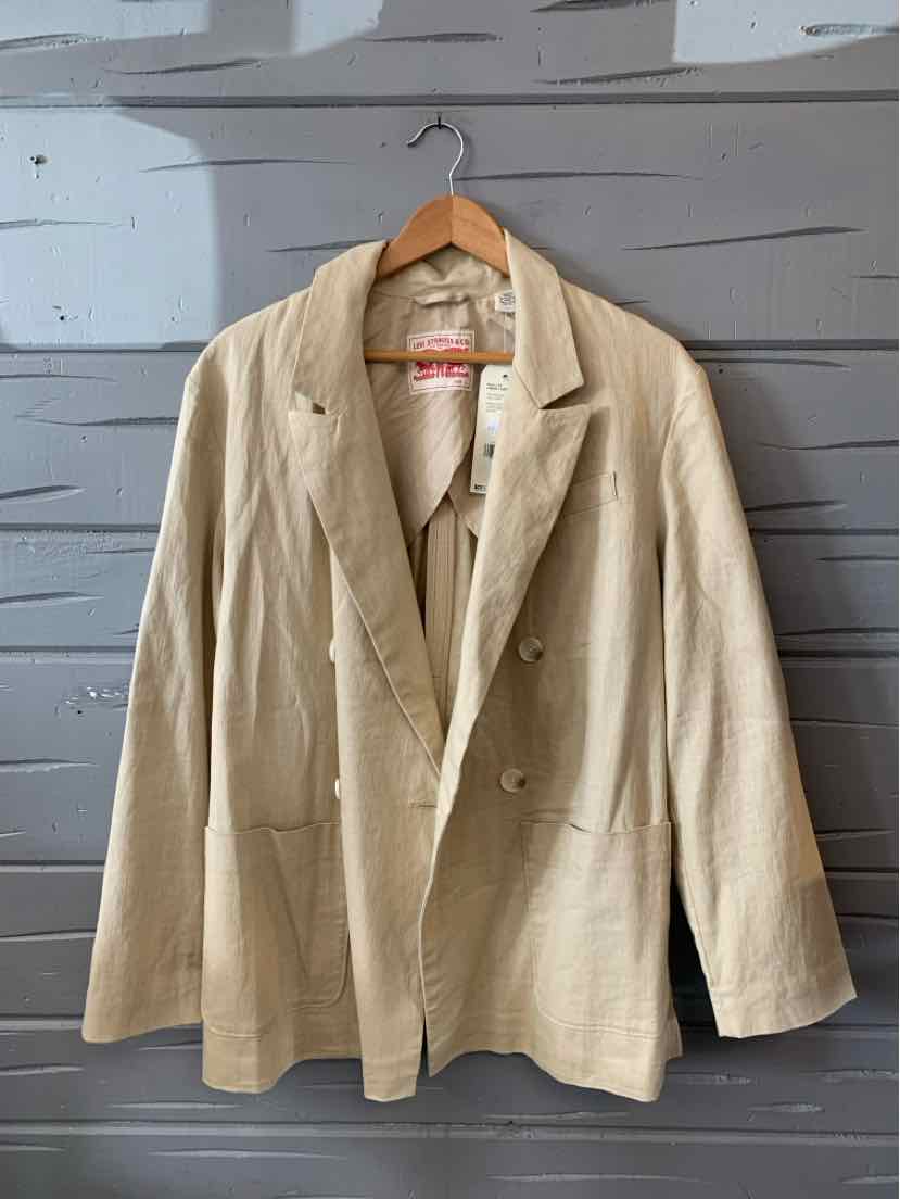 Tan double-breasted blazer with notch lapels and front pockets hanging on wooden hanger.