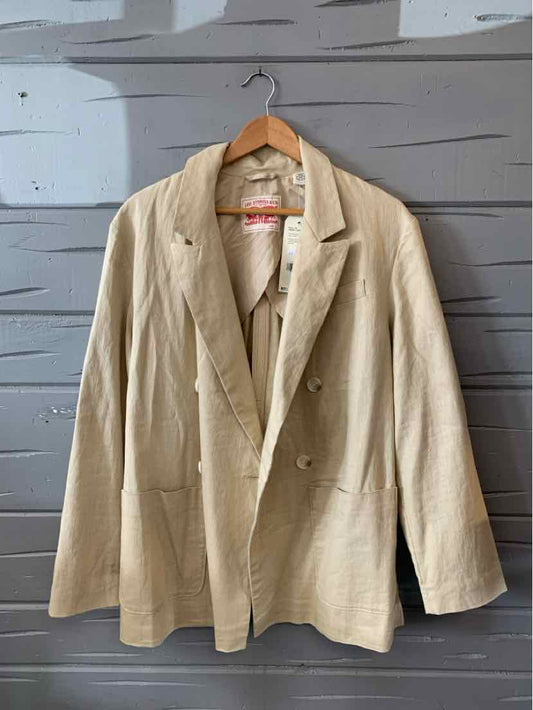 Tan double-breasted blazer with notch lapels and front pockets hanging on wooden hanger.