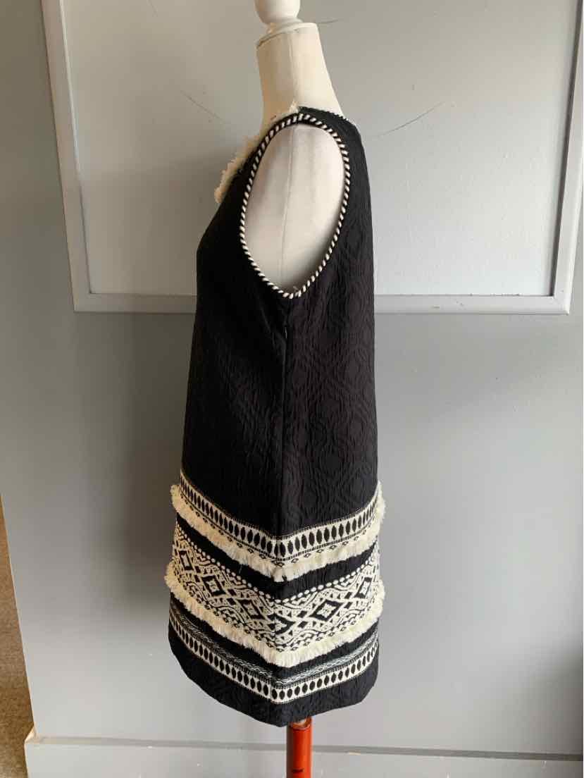 Black sleeveless knit dress with white geometric embroidery and scoop neckline.