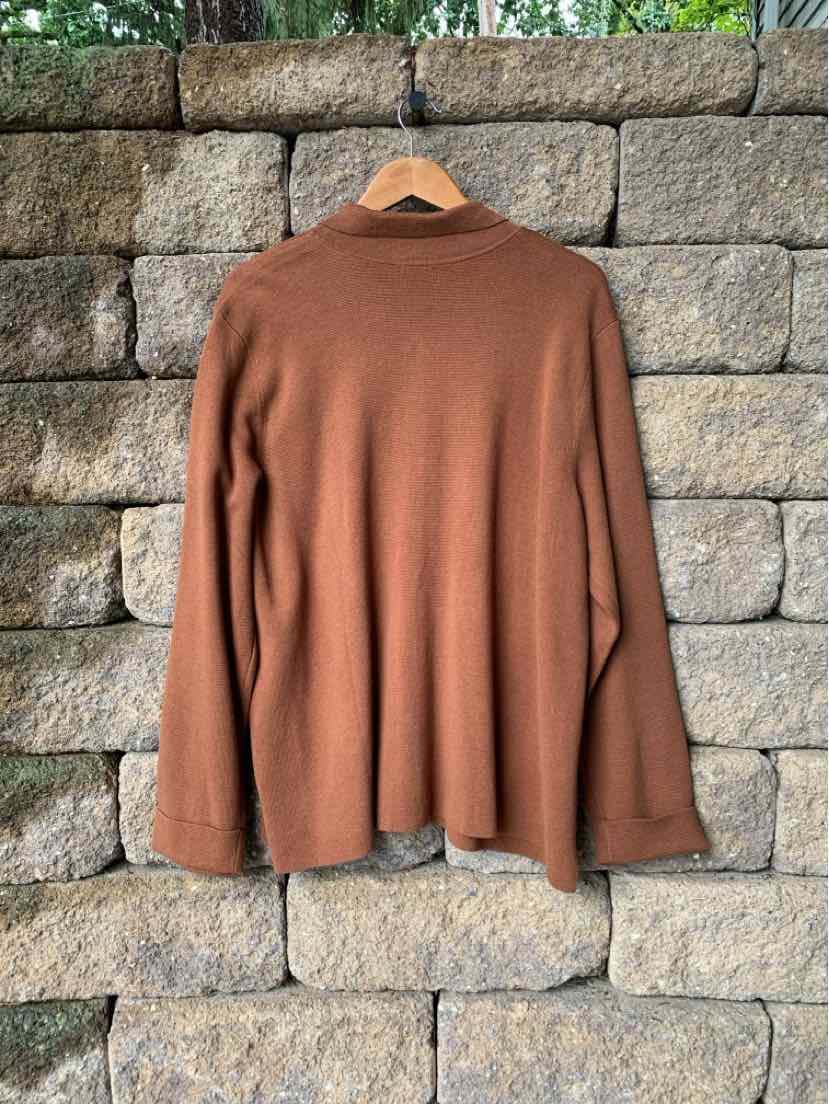 Rust brown oversized knit sweater with long sleeves and a mock neck, hanging on a wooden hanger.