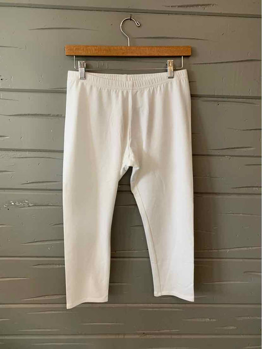 White cropped leggings with elastic waistband and slim fit, hanging on wooden hanger against gray wooden wall.