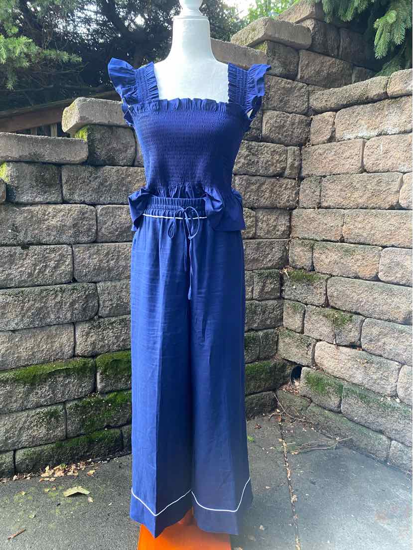 Navy blue sleeveless jumpsuit with ruffled straps and square neckline, cinched waist, wide-leg pants with white trim at hem.