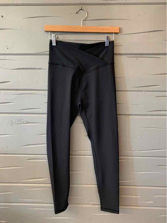 Black high-waisted leggings with a wide overlapping waistband and slim, straight legs, hanging from a clip hanger.
