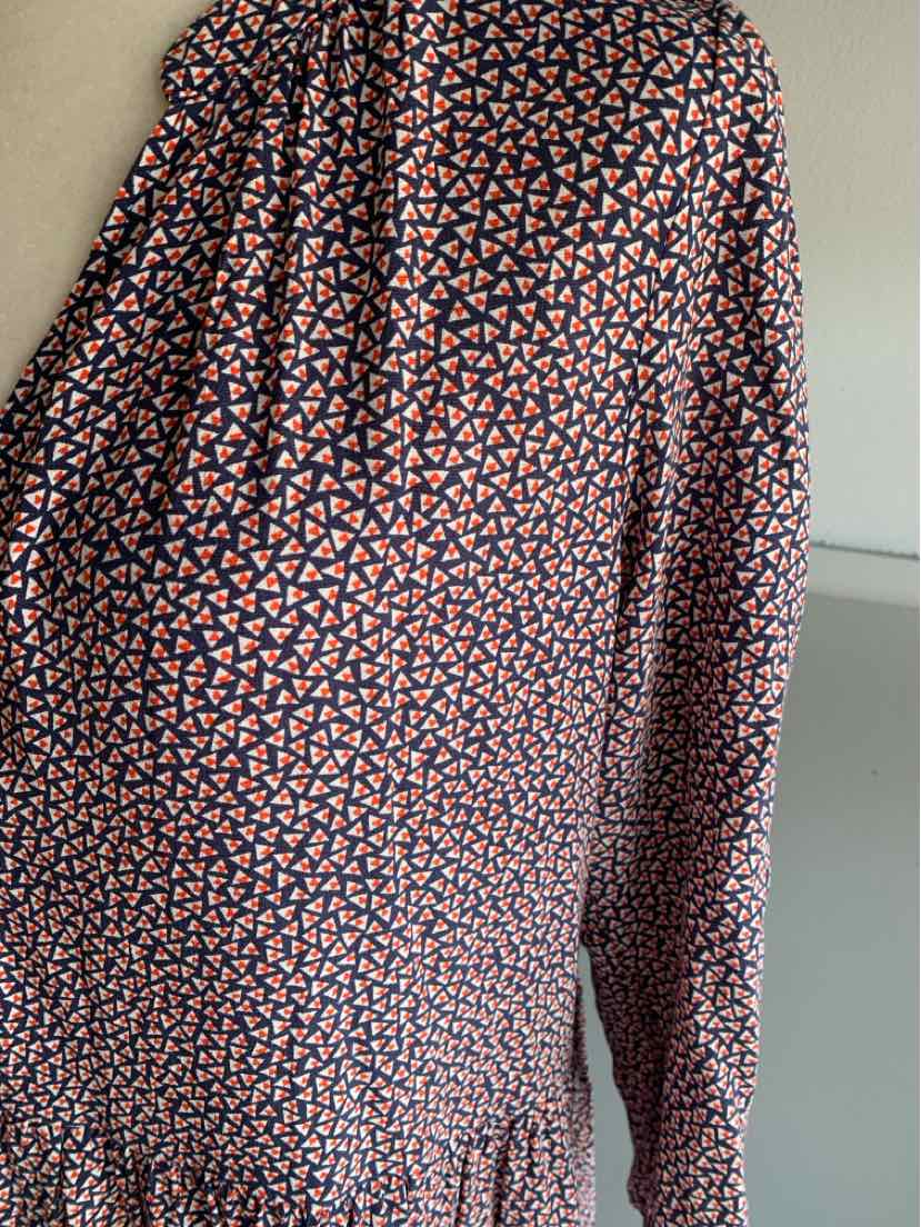 Blue long-sleeve dress with small orange and white geometric pattern, gathered cuff and waist detail.