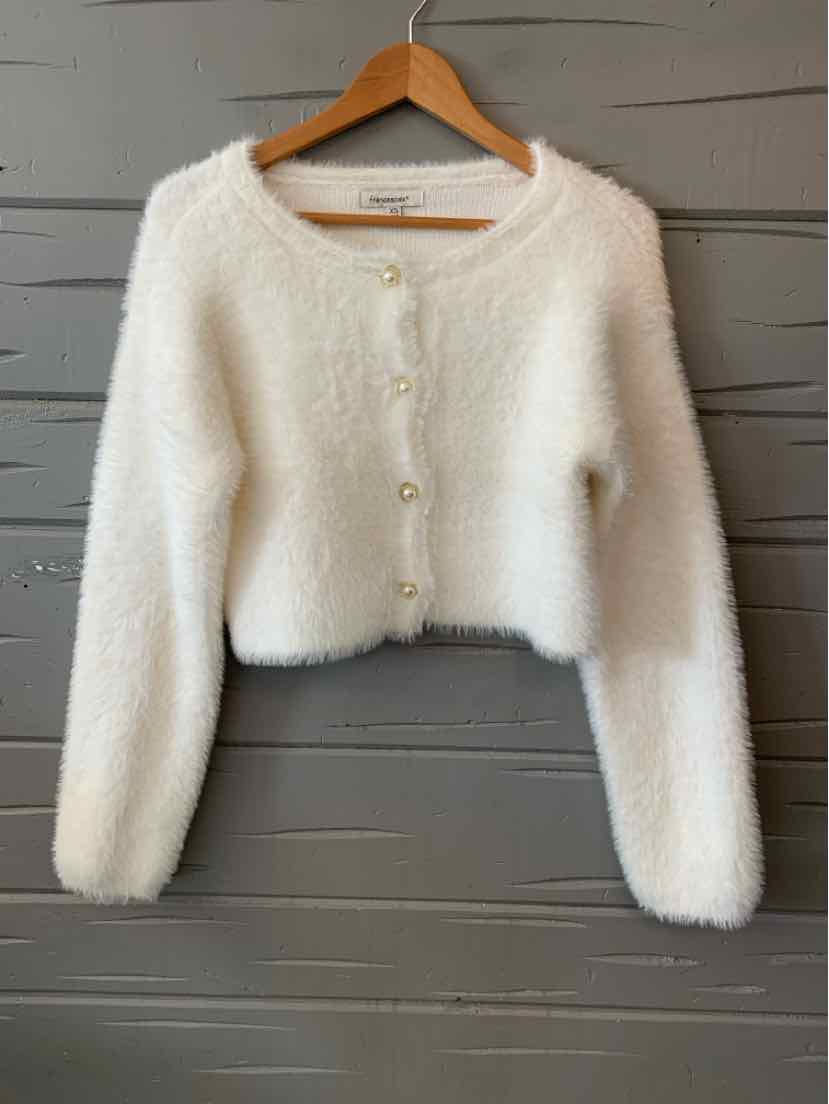 White fuzzy cropped cardigan with long sleeves and pearl-like buttons.