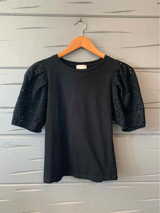Black short-sleeve top with eyelet puff sleeves and crew neckline on wooden hanger.