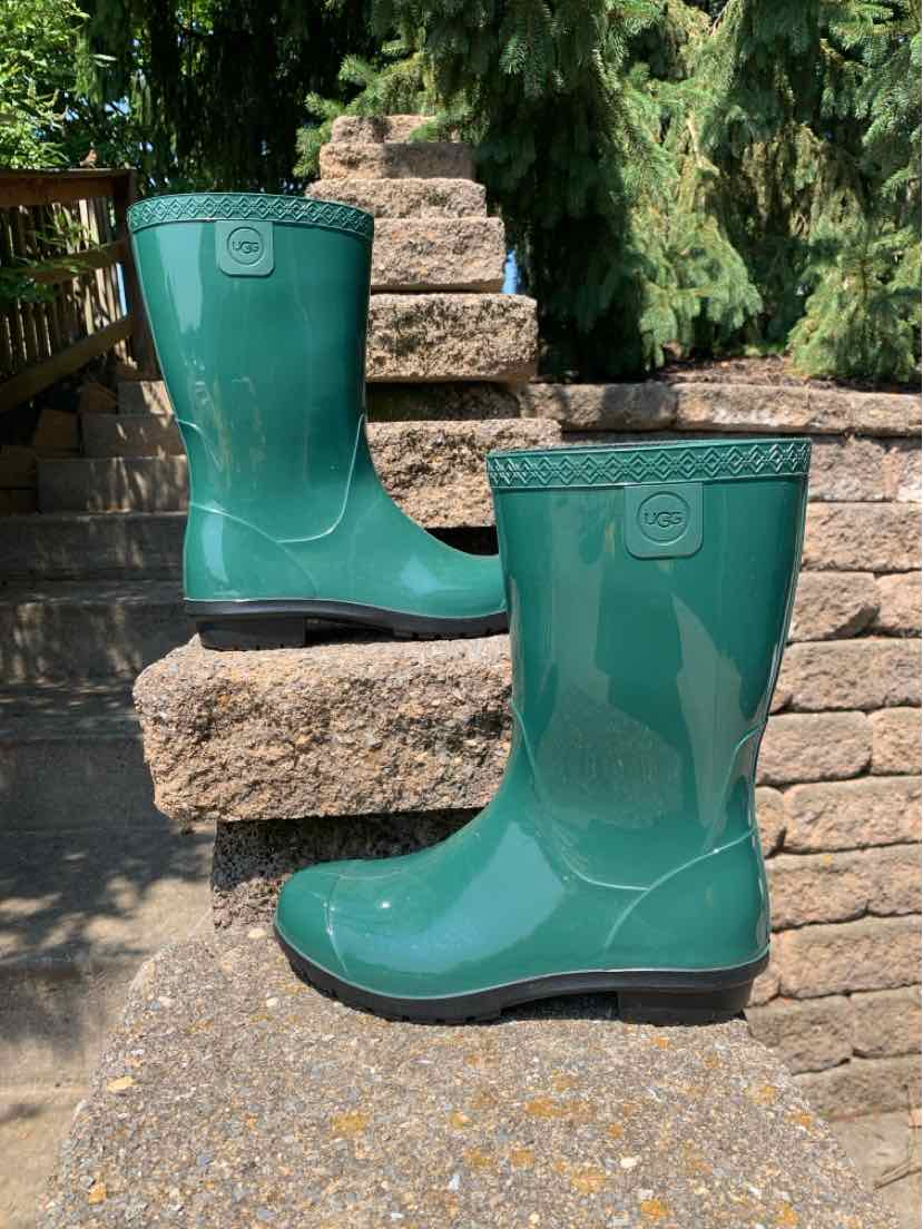 Glossy dark green mid-calf rubber boots with a flat black sole and embossed logo near the top.