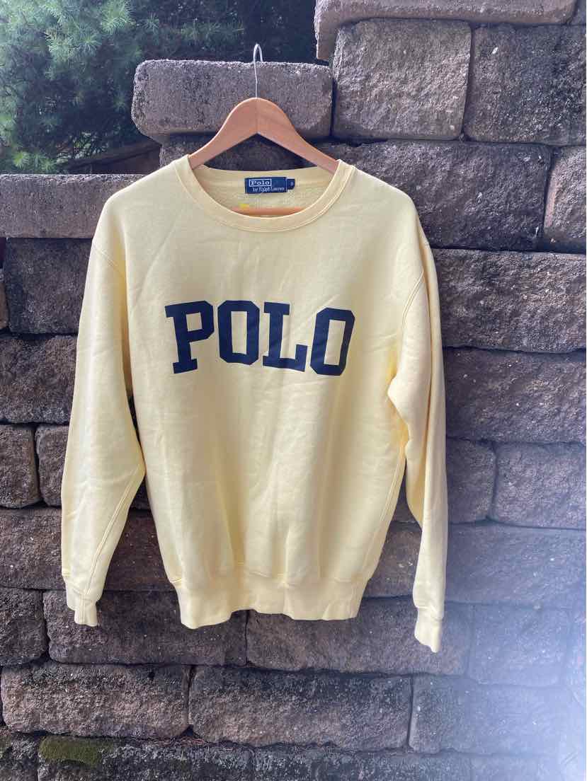 Light yellow crewneck sweater with navy blue "POLO" text across the chest, ribbed cuffs and hem.