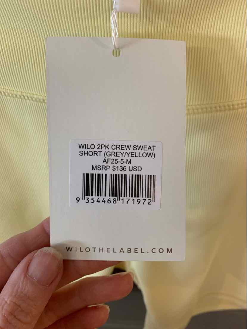 White clothing tag with black text showing product name, size medium, color pastel yellow sweatshirt background.