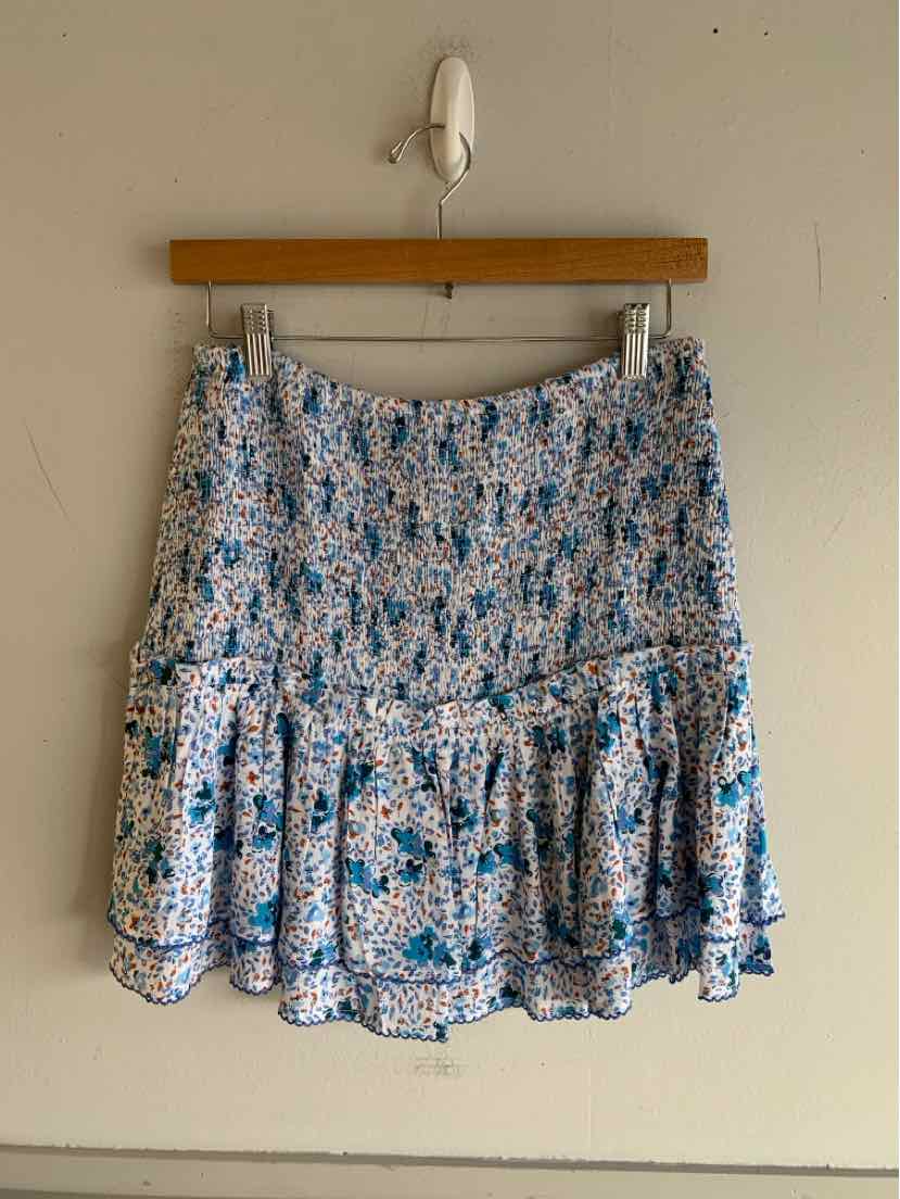 Blue floral smocked mini skirt with ruffled hem hanging on wooden hanger.