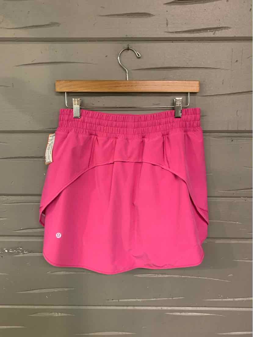 Bright pink athletic skirt with layered design and elastic waistband hanging on wooden hanger.