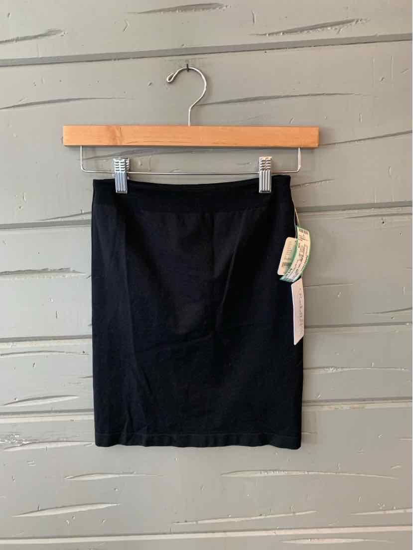 Black fitted mini skirt with side tag hanging on wooden hanger against gray wall.