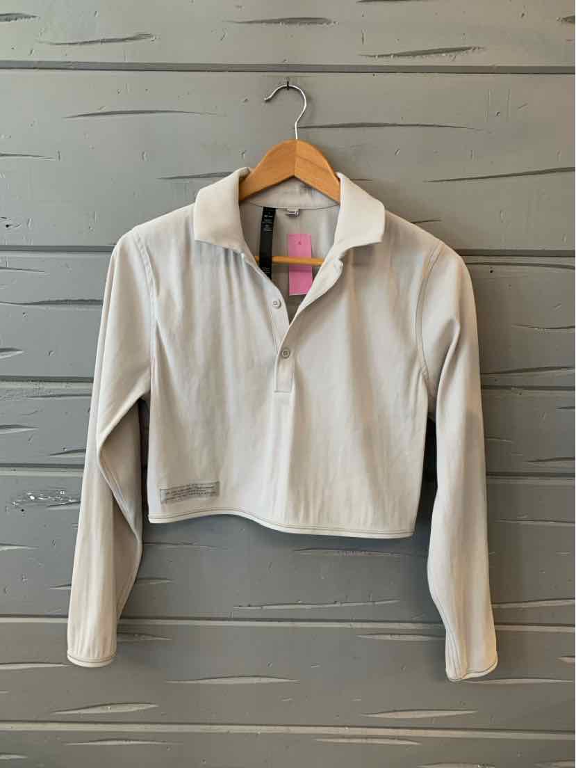 Beige cropped pullover jacket with long sleeves and zippered collar on wooden hanger against gray wood wall.