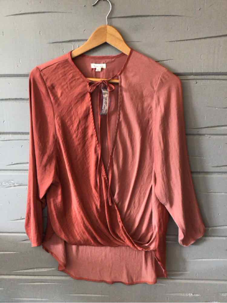 Rust-colored long-sleeve wrap blouse with front tie detail and slightly sheer fabric.