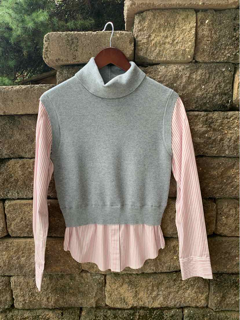 Gray sleeveless turtleneck sweater layered over a light pink long-sleeve button-up shirt with a rounded hem.