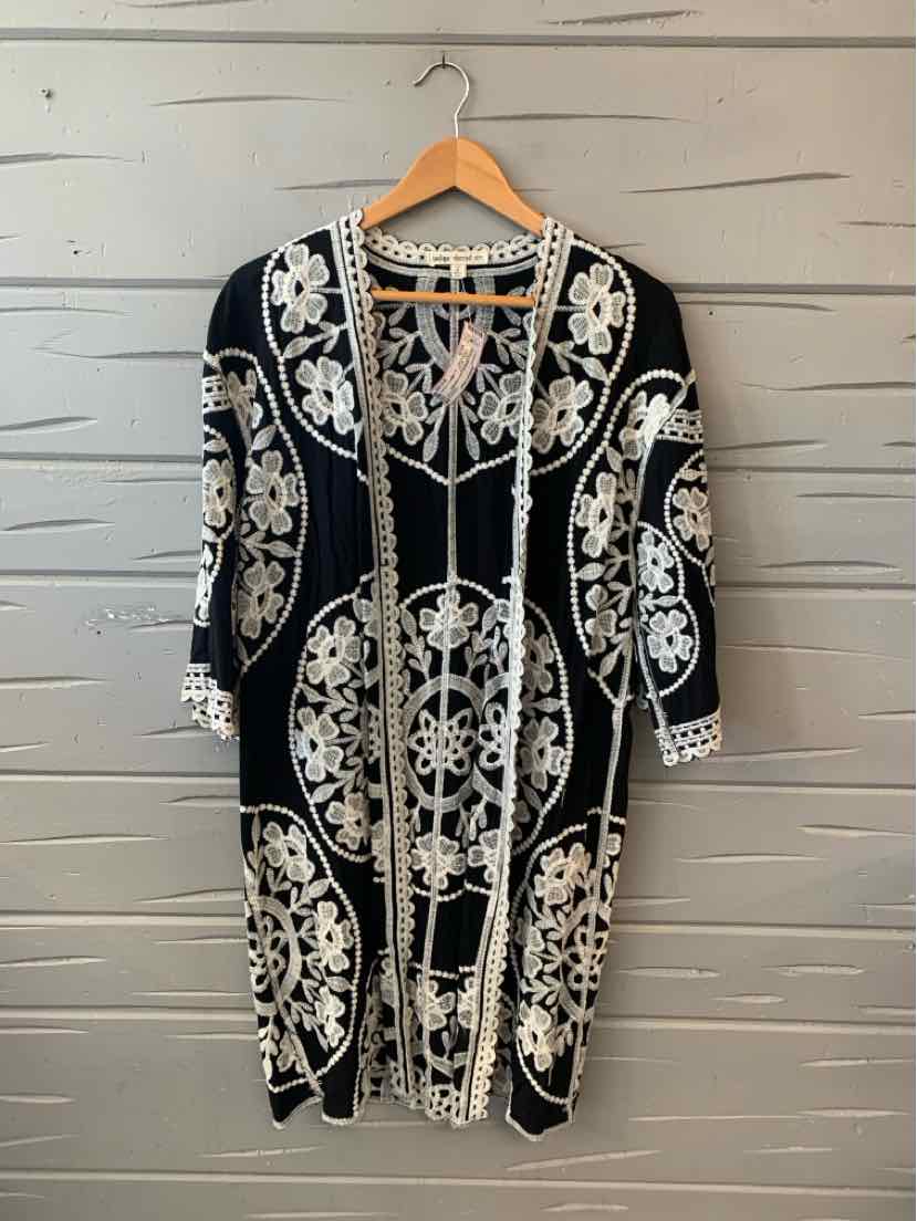 Black knee-length dress with white intricate floral embroidery and three-quarter sleeves on wooden hanger.