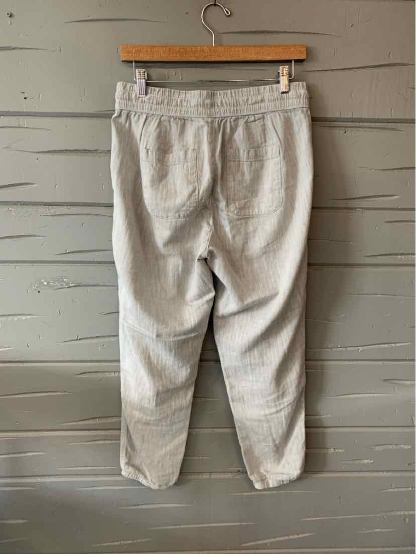 Light gray casual pants with elastic waistband and tapered legs hanging on wooden hanger against gray wood wall.
