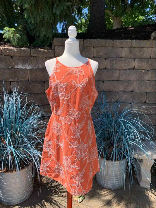 Orange sleeveless dress with white floral print and an adjustable waist tie displayed on a mannequin outdoors.