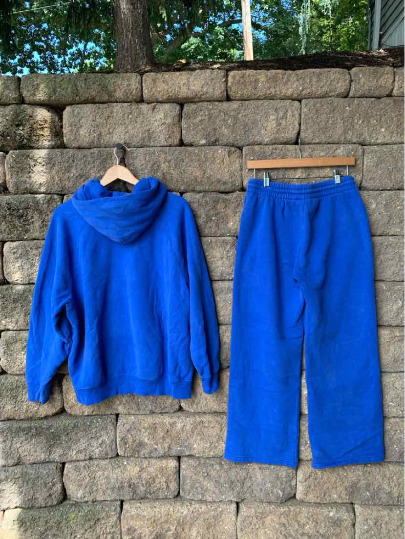 Bright blue fleece hoodie and matching wide-leg pants set hanging against stone wall.