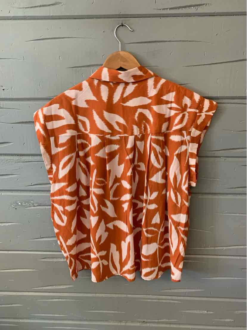Sleeveless orange blouse with white leaf pattern and a collar in size XXL hanging on wooden hanger.
