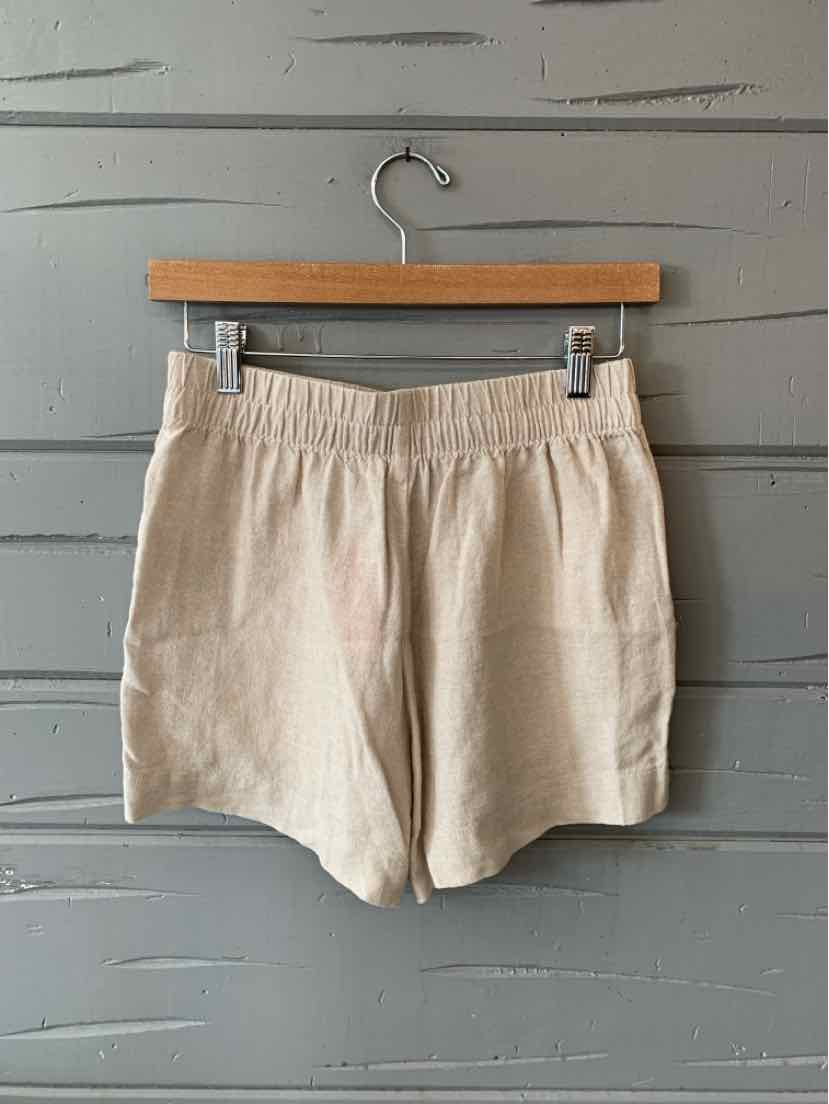 Tan cotton shorts with elastic waistband and relaxed fit hanging on wooden hanger.