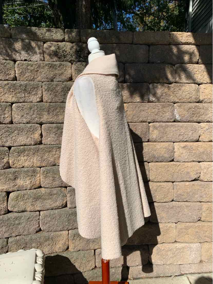 Beige bouclé cape with a high collar and long draped sides, displayed on a mannequin.