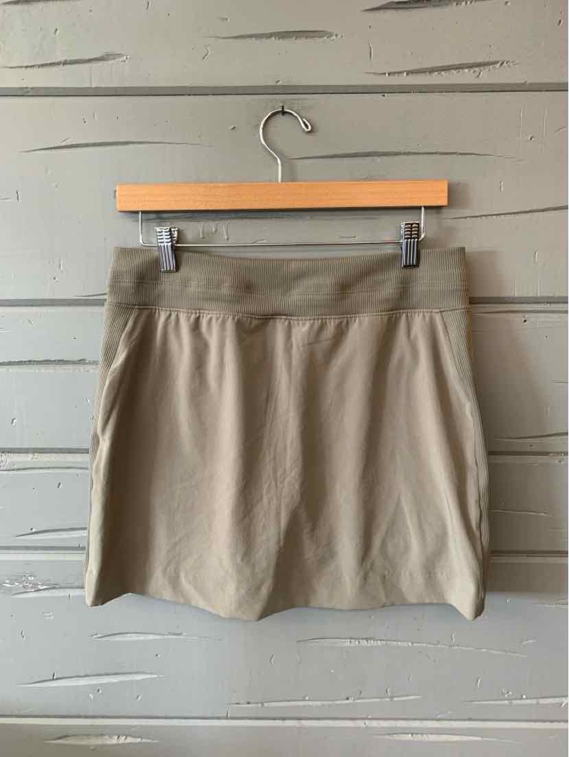 Beige solid mini skirt with elastic waistband hanging on wooden hanger against gray wooden wall.