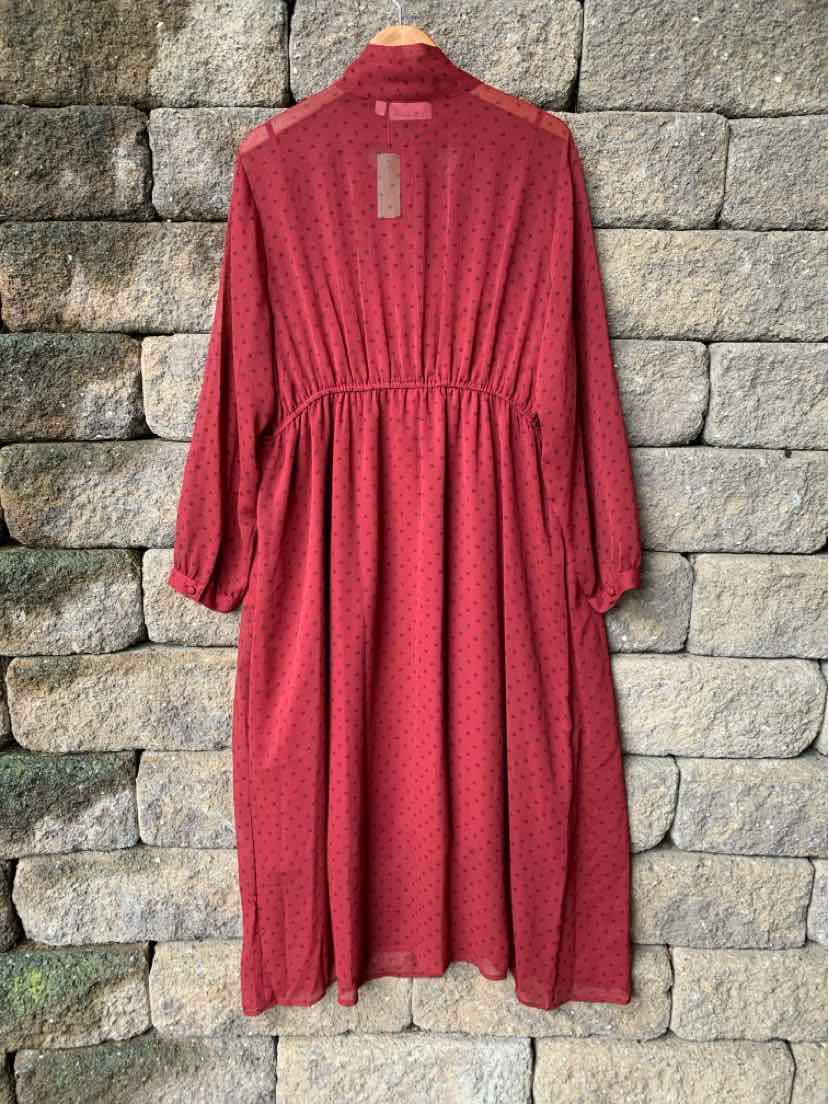 Long-sleeve red dress with subtle dotted pattern, cinched waist, and flowing skirt hanging on wooden hanger.