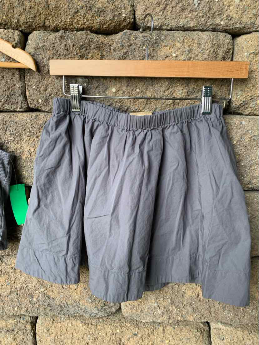 Gray cotton skirt with elastic waistband hanging on wooden hanger against stone background.