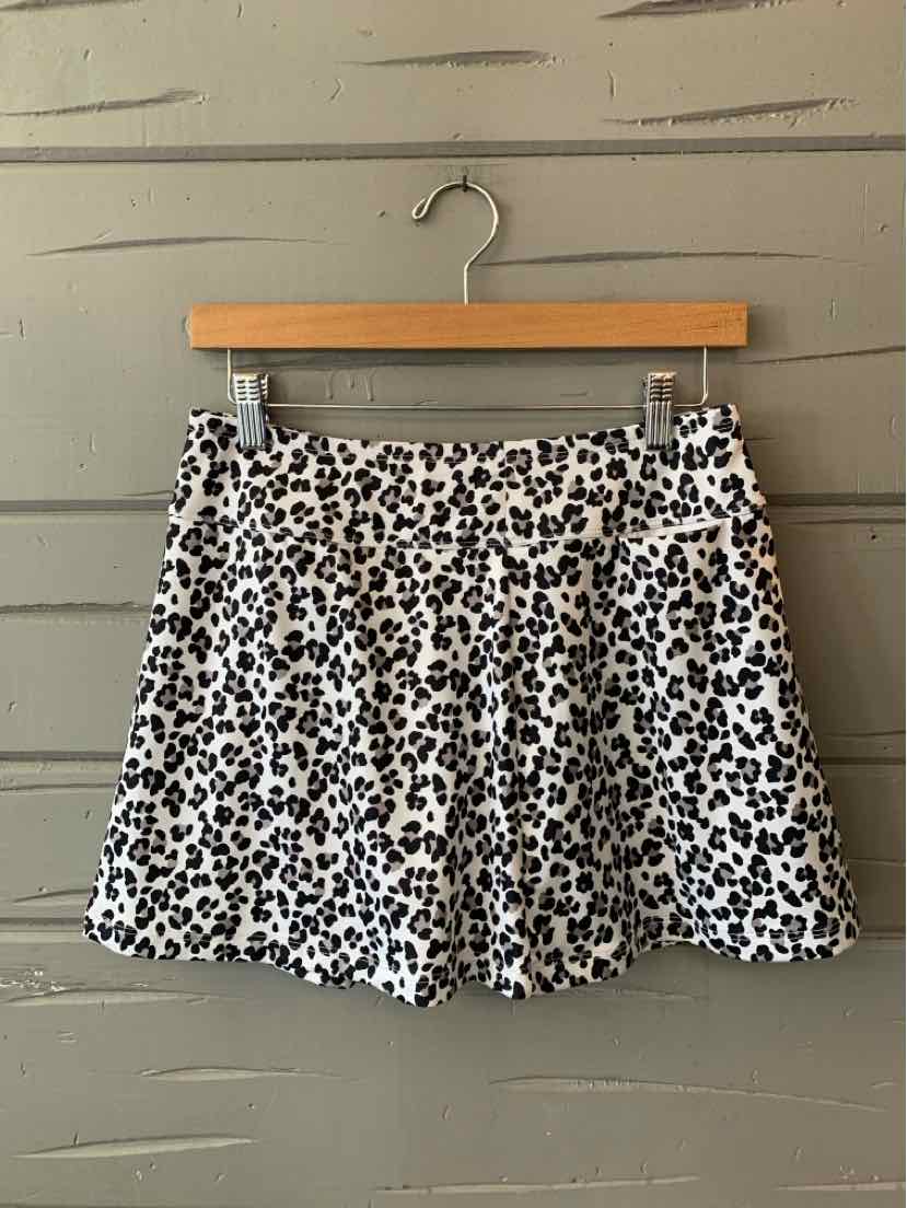 White skirt with black leopard print pattern and a flared silhouette hanging on wooden hanger against gray wall.