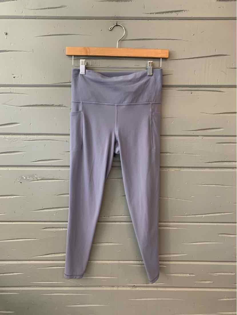Light purple high-waisted athletic leggings with flat seams hanging on wooden hanger against gray wall.