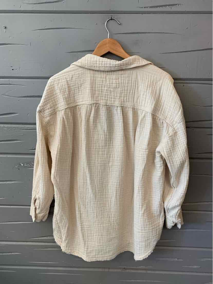 Cream-colored waffle knit long-sleeve shirt with button cuffs hanging on wooden hanger.
