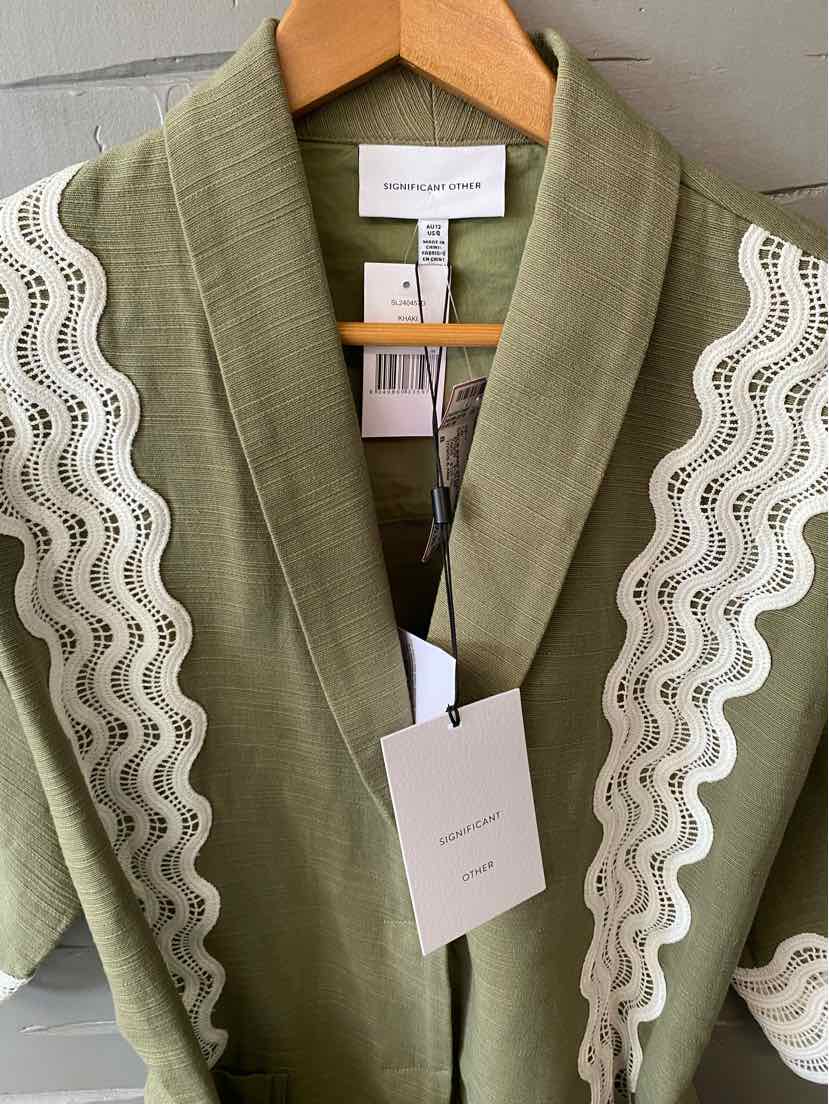 Olive green cardigan with wide shawl collar and white wavy lace trim along the shoulders and front edges.