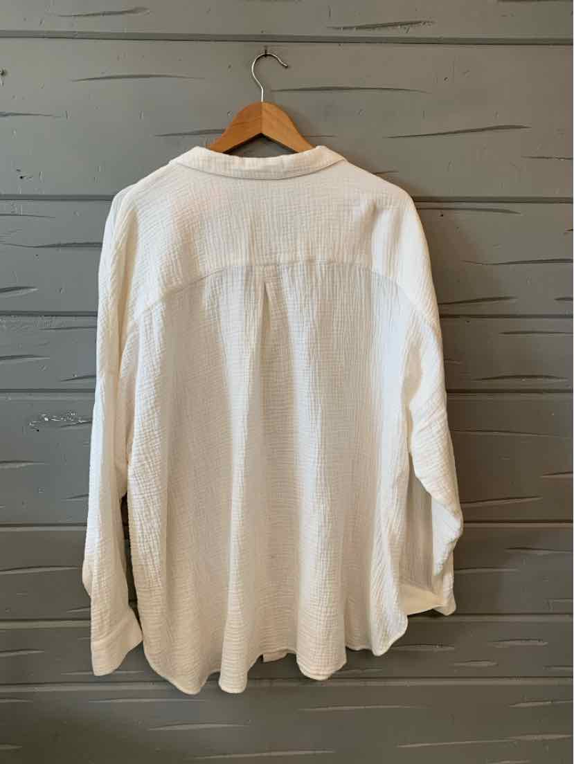 Cream-colored long-sleeve lightweight button-up shirt with a collar hanging on wooden hanger.