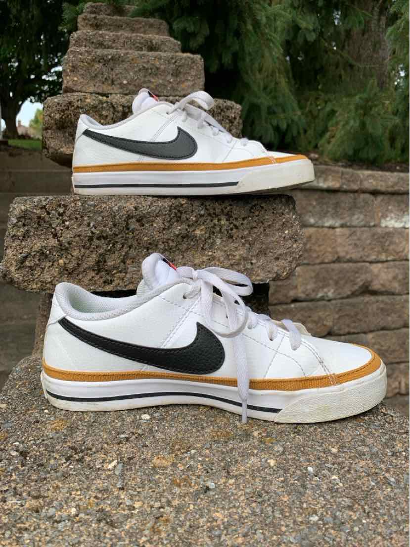 White low-top Nike sneakers with black swoosh, brown trim on sole, and white laces, size 6.5.