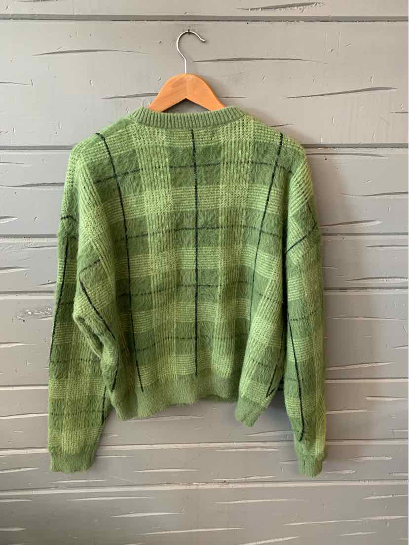 Green plaid sweater with a relaxed fit, ribbed cuffs and hem, hanging on wooden hanger.