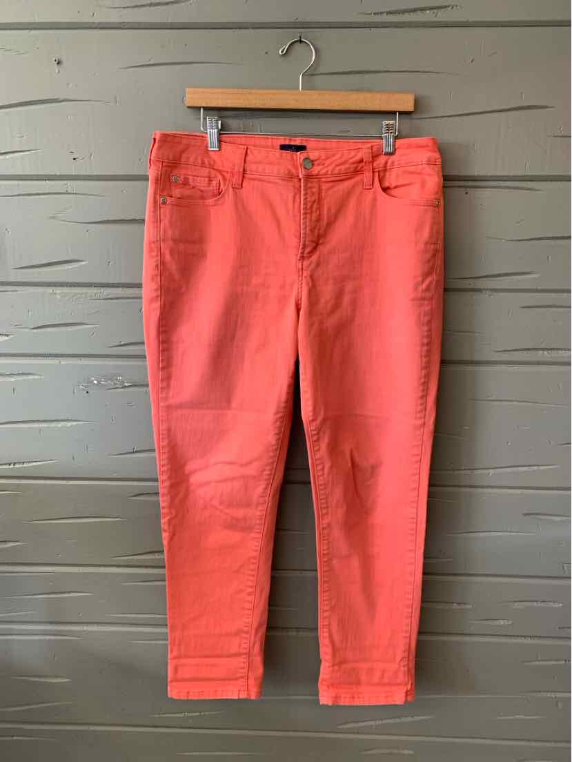 Coral pink straight-leg pants with front pockets and button closure on wooden hanger against gray wall.