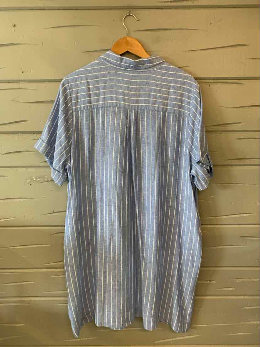 Light blue and white vertical striped oversized shirt dress with short sleeves on wooden hanger against beige wooden wall.