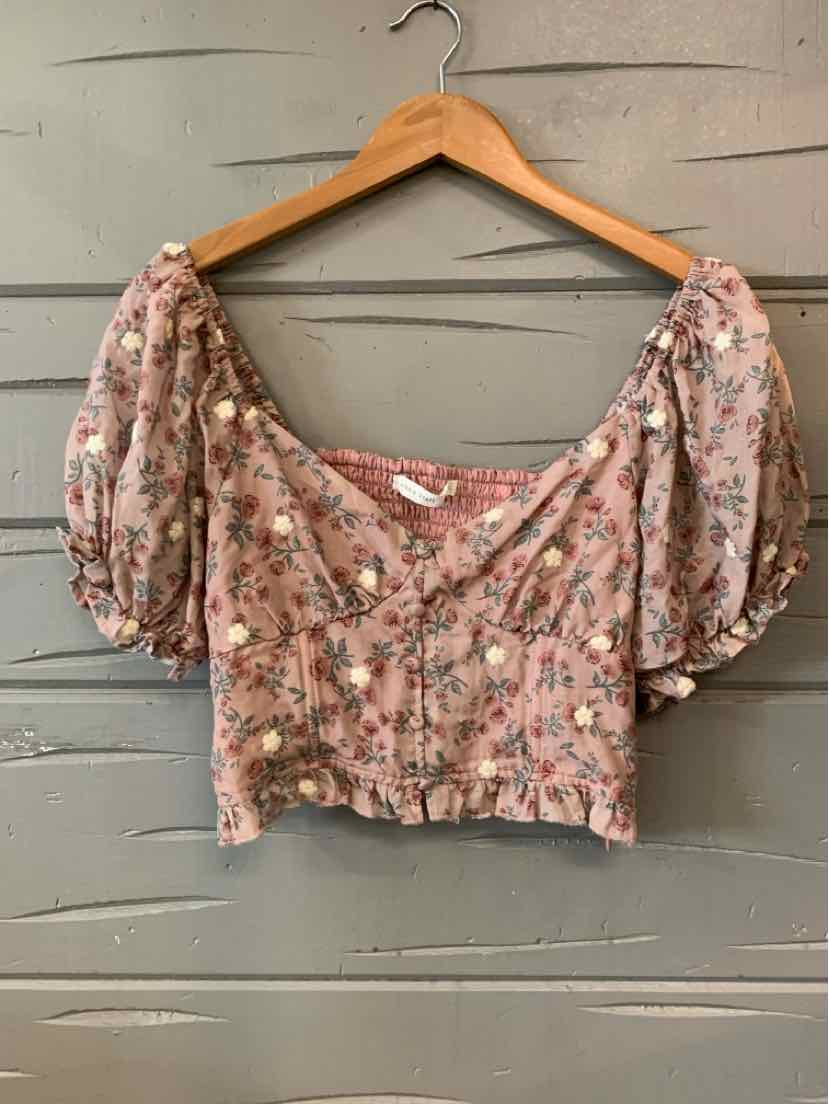 Pink floral cropped blouse with puff sleeves and ruched front on wooden hanger.