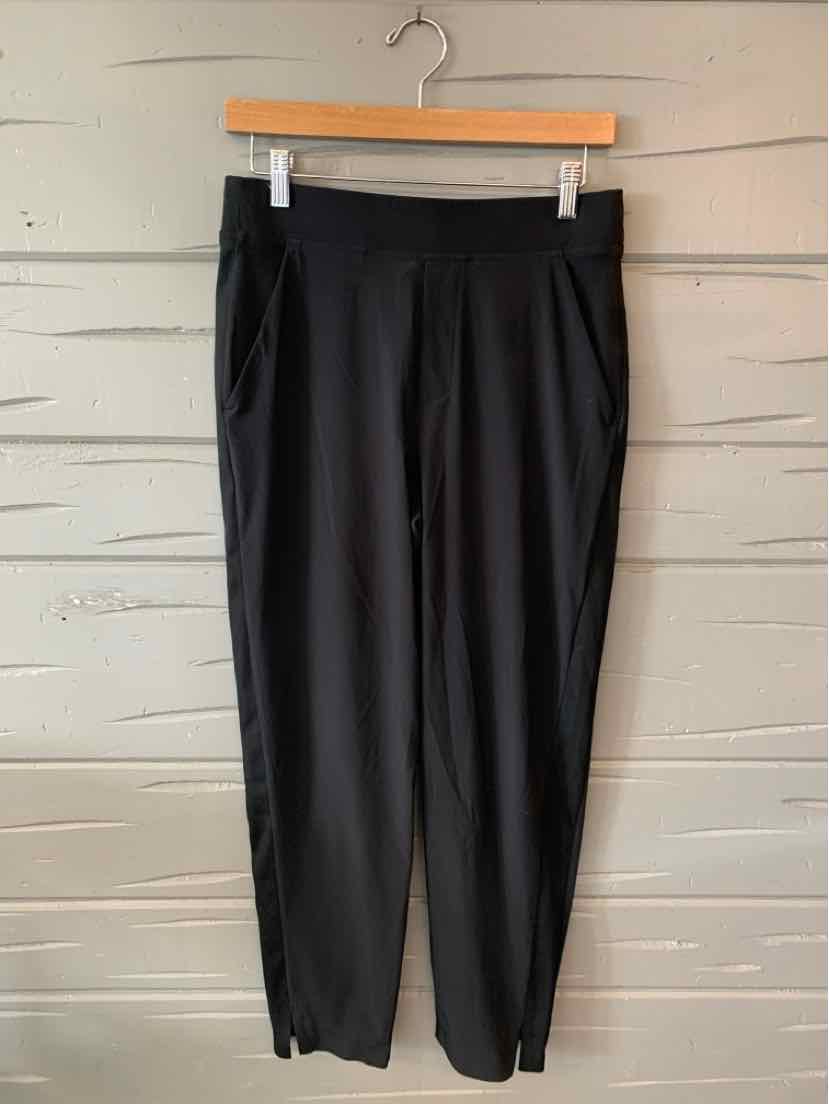 Black high-waist tapered pants with side pockets hanging on wooden hanger.