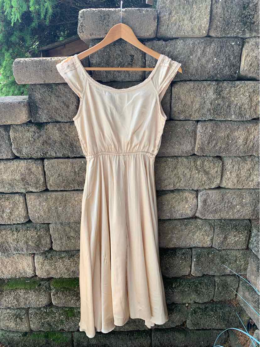 Tan sleeveless dress with scoop neckline, gathered waist, and flowing midi skirt on wooden hanger.