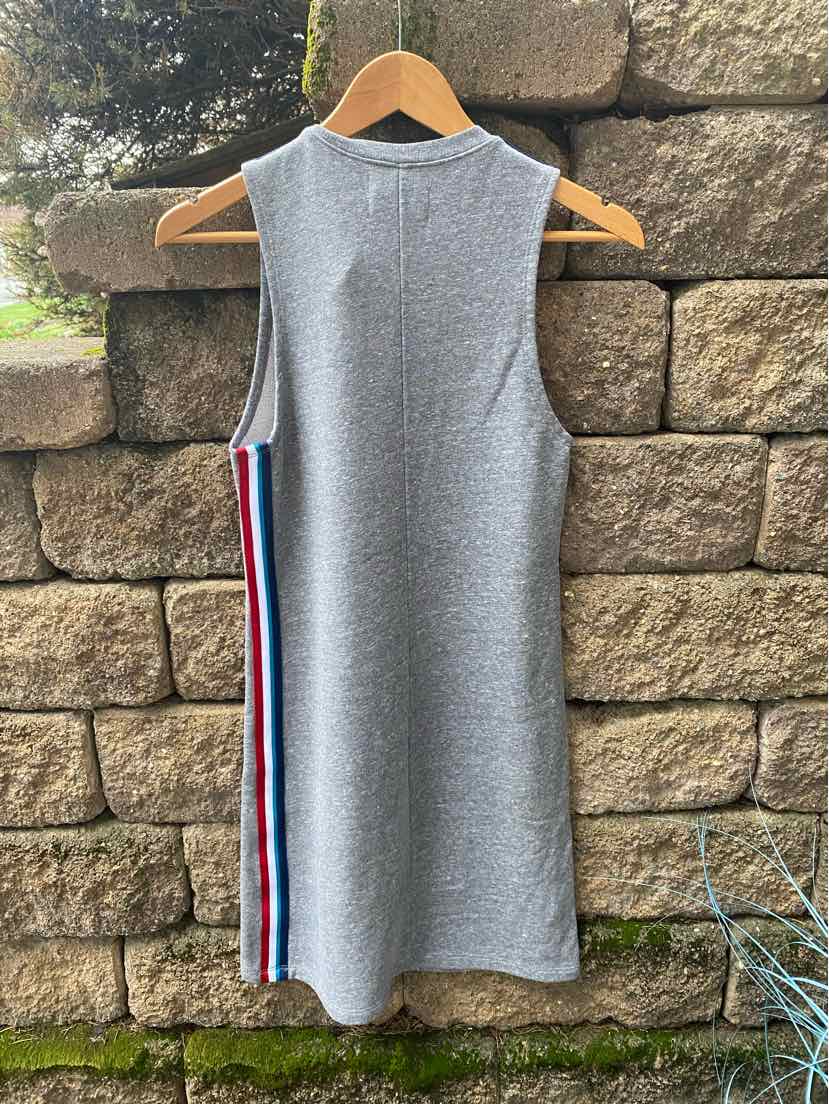 Gray sleeveless knit dress with red, white, and blue side stripes, hung on wooden hanger against stone wall.
